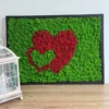 Framed moss wall art featuring two nested hearts design on a wooden surface beside a decorative lantern.