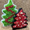 Green and red moss Christmas tree in white frame beside smaller black frame filled with red moss, on cork background