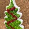 Angled view of white wooden Christmas tree decoration filled with green and red reindeer moss on a cork surface