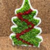 Christmas tree shaped white wooden frame filled with green and red reindeer moss on a cork surface