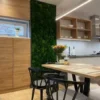 Vertical green moss wall panel installed between wooden cabinets in a modern kitchen dining area