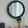 Round framed wall mirror with blue reindeer moss hanging over a vanity with perfume bottles