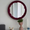 Round mirror with dark red reindeer moss border hanging on a wall above a vanity table.