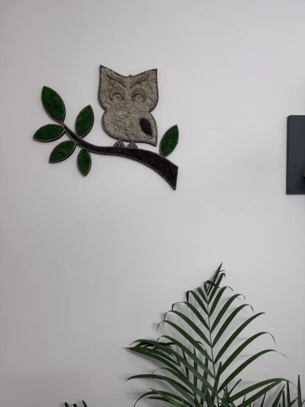 Wall decoration of an owl on a branch made of brown and green moss above a houseplant.