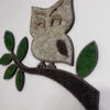 Moss art in owl shape on a branch with green leaves and light moss plumage on a white wall.