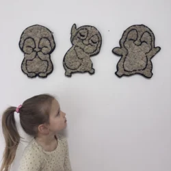 A small girl looks at three fluffy penguin-shaped wall decorations on a white wall.