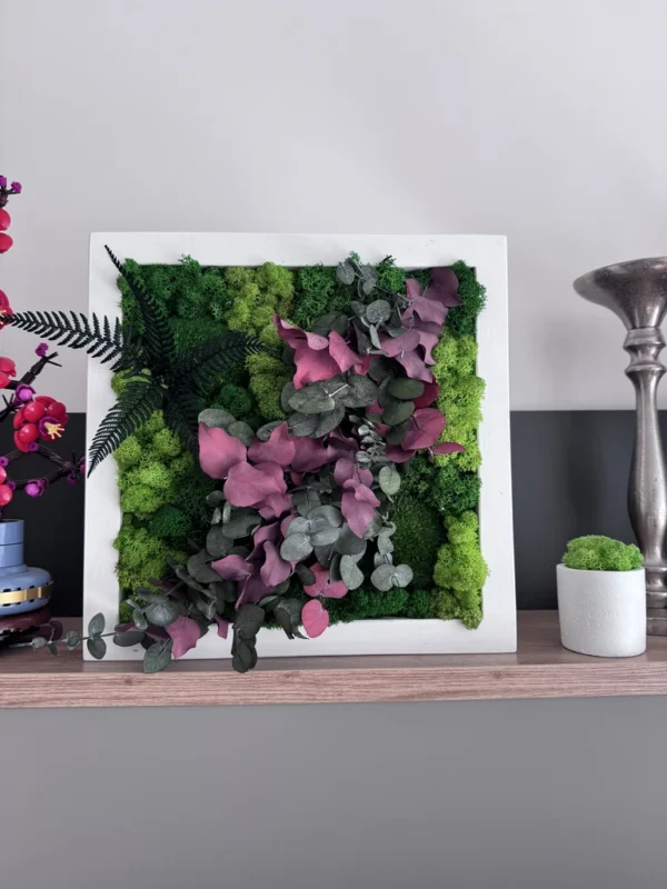 IMG_8677_result Square plant wall art with green reindeer moss, fern, and red eucalyptus leaves in a white frame on a wooden shelf.