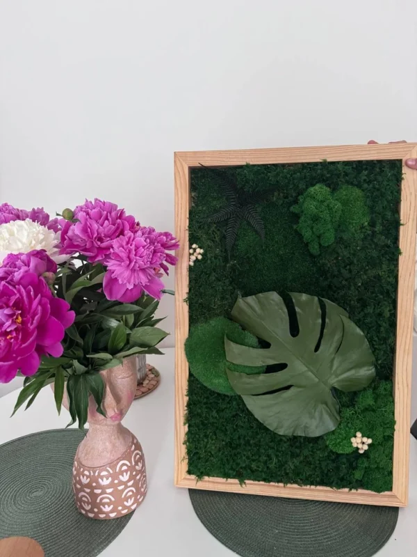 photo_2026-07-06_10-54-10_result Moss art with Monstera leaf in a wooden frame, placed next to a vase with pink peonies.